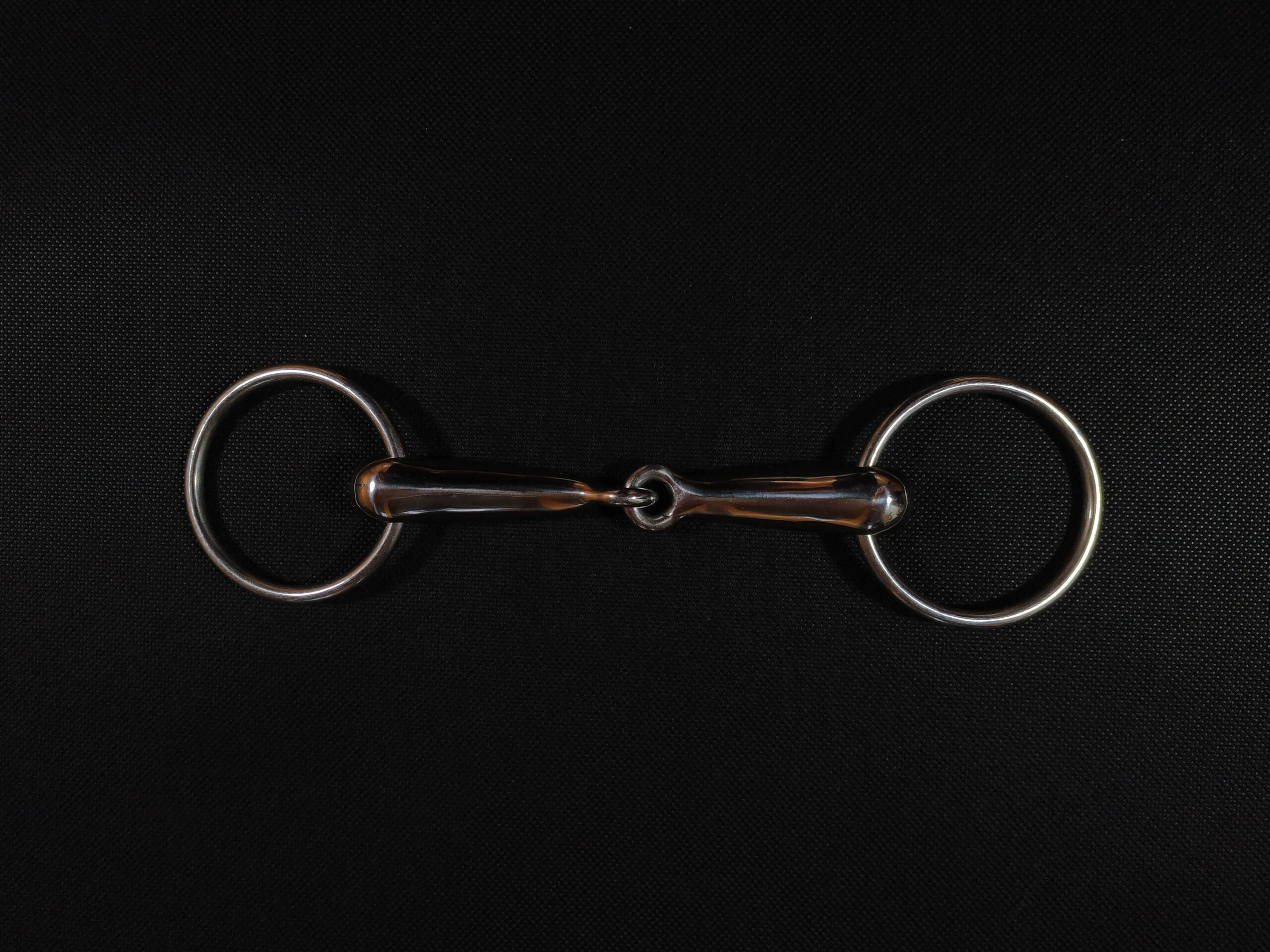 A single jointed snaffle bit against a black background - HQ Pony Magazine
